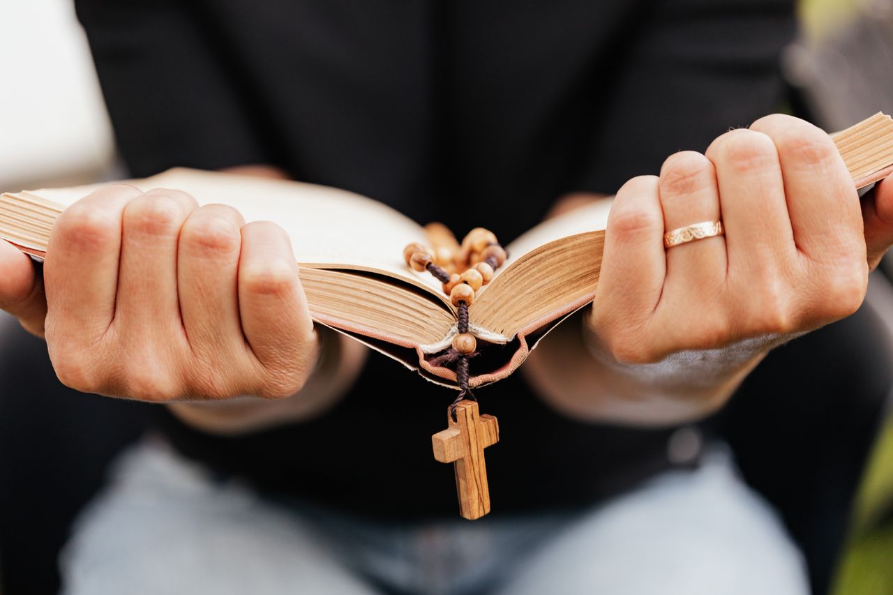 About A close-up of hands holding an open Bible with a rosary, symbolizing faith.